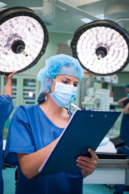 Weiblicher Chirurg, der auf Zwischenablage im Operationssaal schreibt