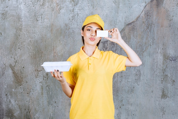 Weiblicher Dienstagent in der gelben Uniform, die eine Plastikbox zum Mitnehmen hält und ihre Visitenkarte präsentiert.