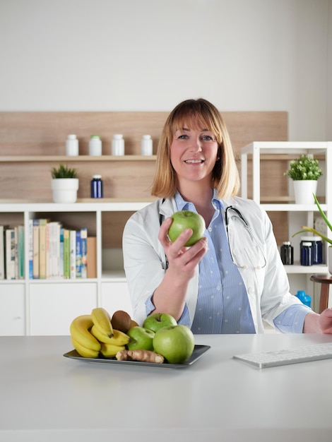 Weiblicher Ernährungswissenschaftler, der einen grünen Apfel im Bürostudio hält