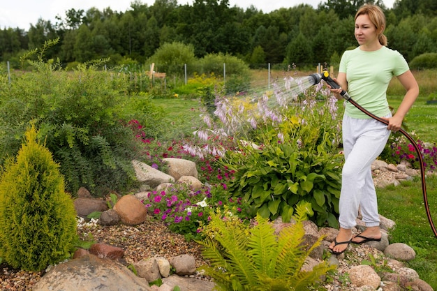 Weiblicher Gärtner, der Blumen in einem Blumenbeet mit einem Gartenschlauch gießt