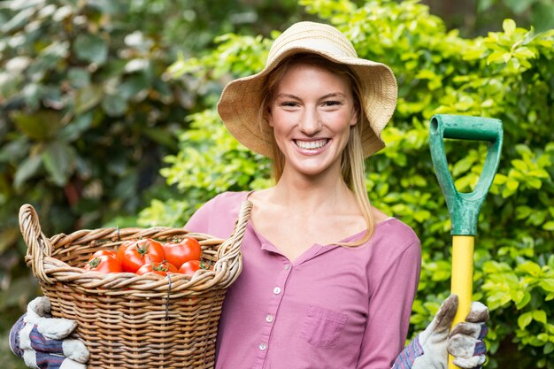 Weiblicher Gärtner, der Tomatenkorb und Arbeitswerkzeug hält