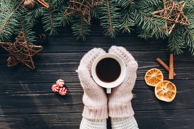 Weiblicher haltener Schalenkaffee. Weihnachtsdekoration und -lebensmittel auf hölzernem Hintergrund.