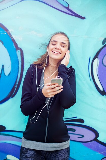 Weiblicher Jogger, der Musik auf Handy vor Graffiti-Wand hört