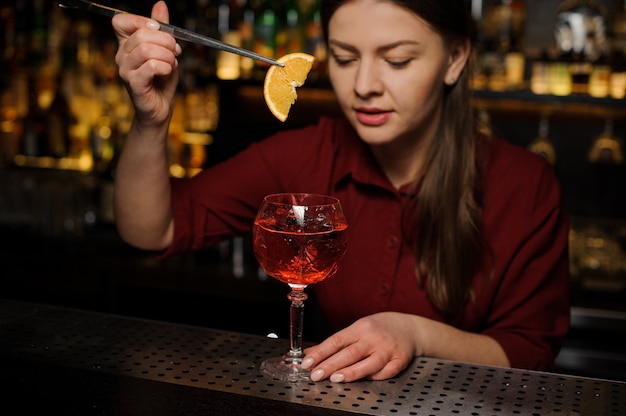 Weiblicher Kellner, der eine Scheibe der Orange in ein Glas Aperol-Spritzencocktail setzt