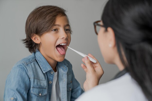 Weiblicher Kinderarzt, der ein digitales Thermometer verwendet, um die Temperatur des kleinen Jungen zu überprüfen