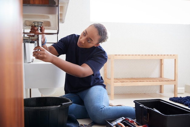 Weiblicher Klempner, der daran arbeitet, ein undichtes Waschbecken im Badezimmer zu reparieren