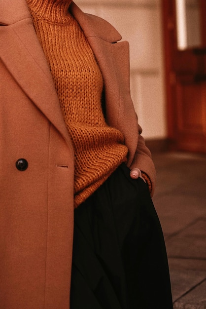 Weiblicher Körper im orangefarbenen, warmen Strickpullover und langen braunen Mantel. Herbst-Winterkleidung