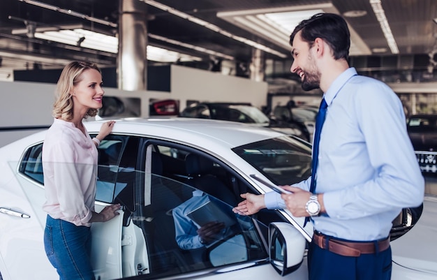 Weiblicher Kunde und lächelnder Verkäufer, der neues Auto im Händlersalon betrachtet