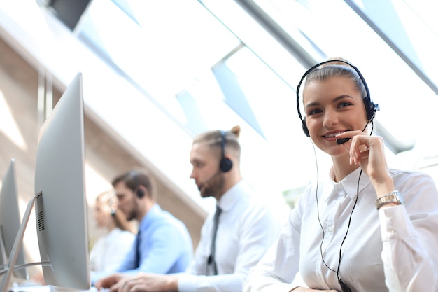 Weiblicher Kundendienstmitarbeiter mit Headset und lächelnd, begleitet von ihrem Team.