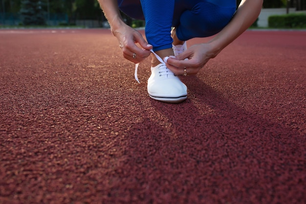 Weiblicher Läuferathlet, der weiße Laufschuhe auf der Laufstrecke bindet. Platz für Text