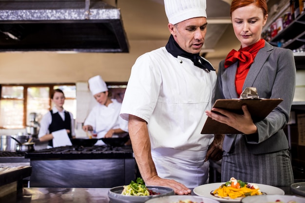 Weiblicher Manager und männliches Chefschreiben auf Klemmbrett in der Küche