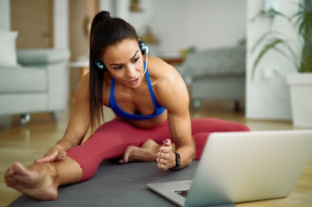 Weiblicher persönlicher Trainer, der Dehnübungen macht, während er zu Hause auf dem Laptop vloggt