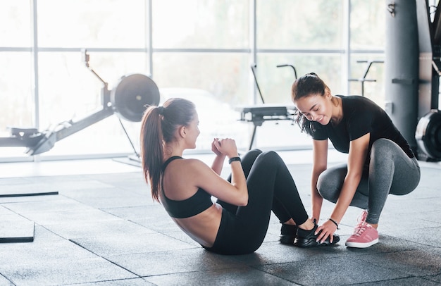 Foto weiblicher personal trainer, der jungen frau hilft, übungen im fitnessstudio zu machen.