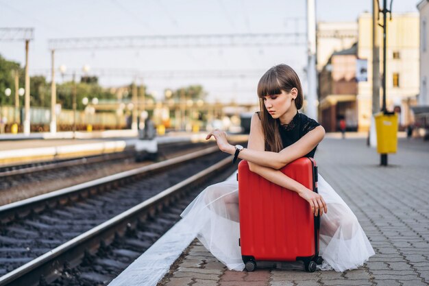 Weiblicher Reisender mit rotem Koffer, der Zug am Bahnhof wartet