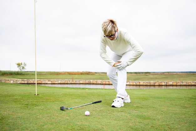 Weiblicher Senior Golfspieler mit gesundheitlichen Problemen und Knieschmerzen beim Golftraining.