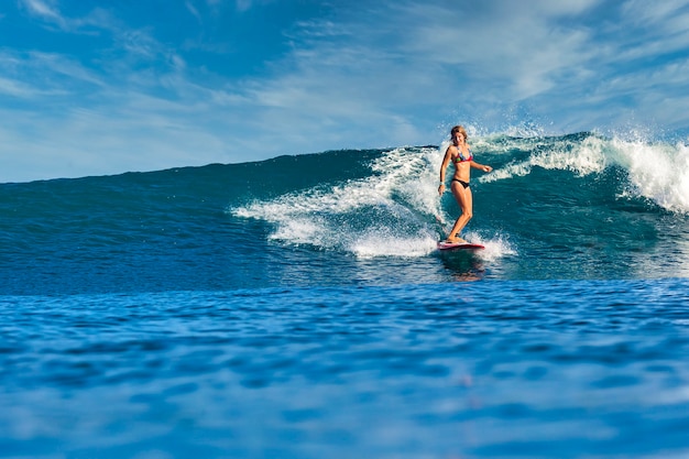 Weiblicher Surfer auf einer blauen Welle am sonnigen Tag