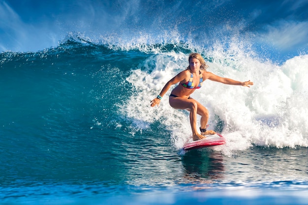 Weiblicher Surfer auf einer blauen Welle am sonnigen Tag