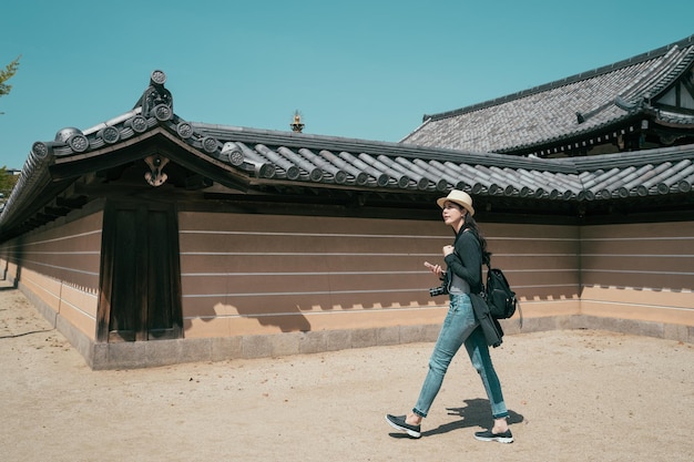 weiblicher tourist, der an der riesigen und langen wand von shitennoji osaka japan spaziert. in voller länge von reisenden rucksackreisenden, die handy und kamera im freien halten und an einem sonnigen tag zur nächsten touristenattraktion gehen.