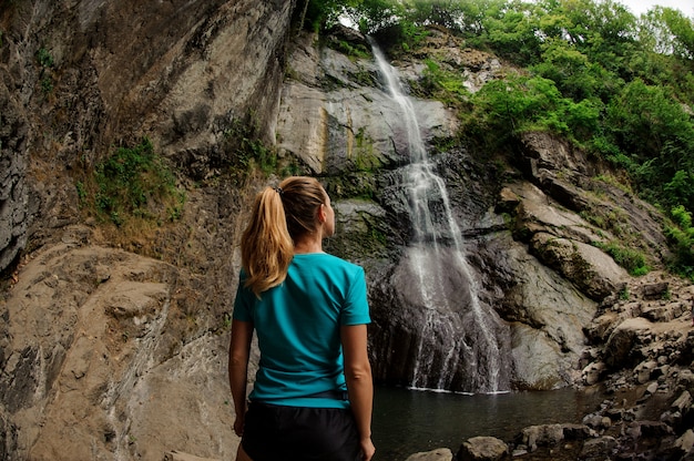 Weiblicher Tourist in der Sportkleidung, die nahen Wasserfall steht