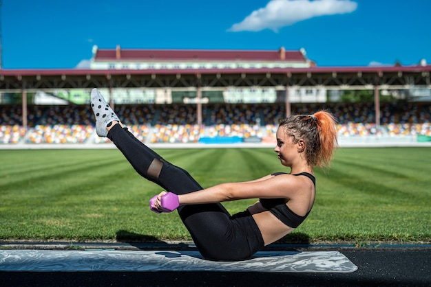 Weiblicher Trainer, der Yoga oder Pilates-Übungen vor grünem Stadionhintergrund macht Aktiver Lebensstil gesund