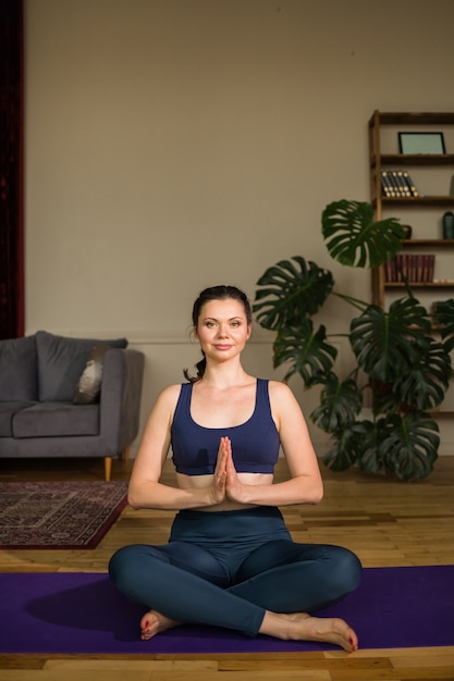 Weiblicher Yogi in Sportbekleidung sitzt in einer Lotussitzposition auf einer Yogamatte in einem Raum