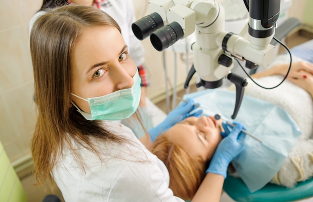 Weiblicher Zahnarzt, der Karies unter Verwendung des Mikroskops im Zahnarztbüro behandelt