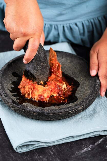 Weibliches asiatisches handzerkleinertes Fried Chicken mit würziger Chilipaste mit indonesischem Mörser und Stößel, Prozessherstellung oder Kochen Ayam Geprek, beliebtes Street Food in Indonesien.