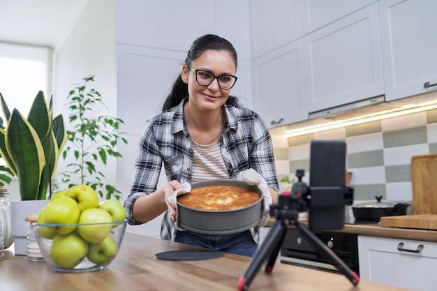 Weibliches Aufnahmevideo eines Apfelkuchenrezepts auf dem Smartphone zu Hause in der Küche