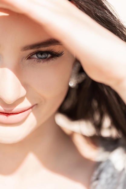 Weibliches frisches Sommerporträt eines schönen glücklichen Mädchens mit blauen Augen halbes Gesicht Die schöne Frau deckt ihre Augen vom Sonnenlicht ab und schaut in die Kamera Schönheit und Sommer