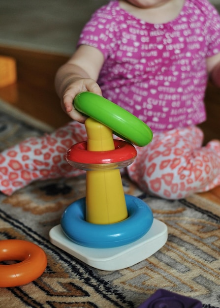 Weibliches Kleinkind sitzt auf dem Boden des Wohnzimmers und spielt mit Spielzeugbauringen. Kleinkind-Stapelringe