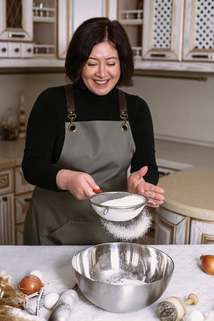 Weibliches Kochen in der Schürze sieben Mehl in einer Metallschale