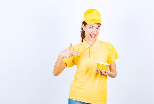 Weibliches Mädchen in gelber Uniform, das eine gelbe Nudelschale zum Mitnehmen hält.