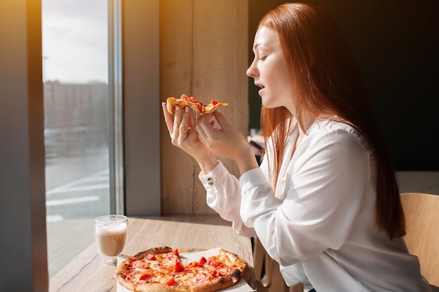 Weibliches Model hält ein Stück Pizza in den Händen. Junge Frau, die Pizza im Café isst.