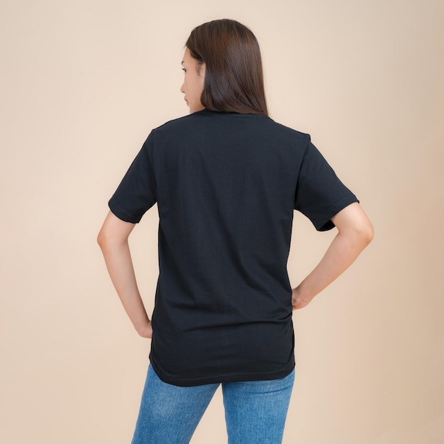 Weibliches Model in schwarzem T-Shirt und Jeans steht im Studio auf beigem Hintergrund