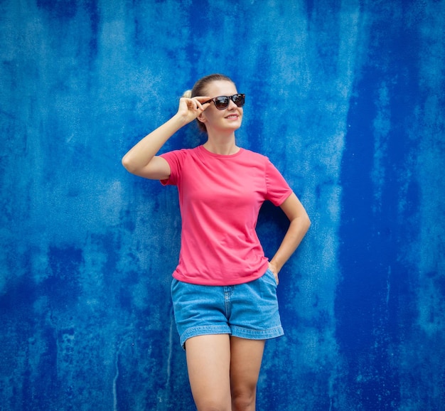 Weibliches Model trägt rosa leeres T-Shirt auf dem Hintergrund einer blauen Wand