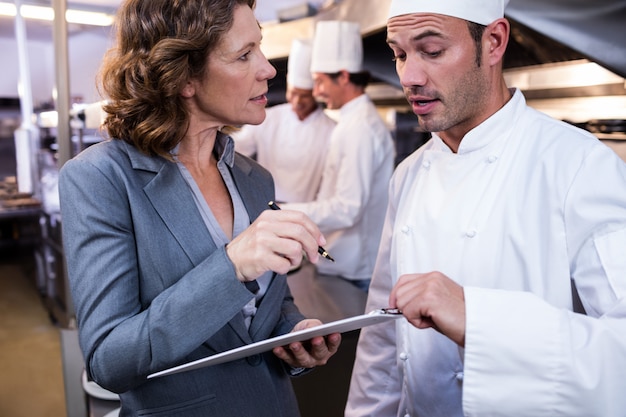 Weibliches Restaurantmanagerschreiben auf Klemmbrett bei der Interaktion mit Küchenchef