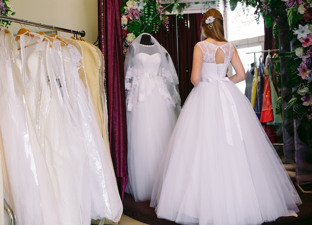 Weibliches versuchen auf hochzeitskleid in einem shop mit frauenassistent.