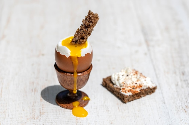 Weich gekochtes Ei im Eierbecher mit Scheibe geröstetem Toast auf weißem Holztischhintergrund