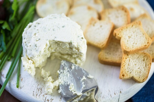 Weicher aromatisierter Rahmkäse mit Knoblauch und feinen Kräutern auf einem Holzbrett mit Crackern.