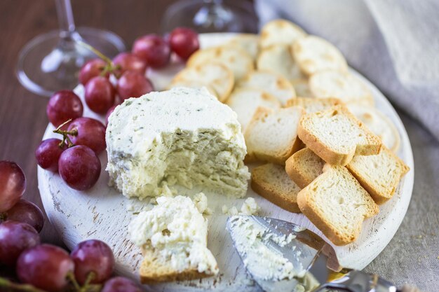 Weicher aromatisierter Rahmkäse mit Knoblauch und feinen Kräutern auf einem Holzbrett mit Crackern.