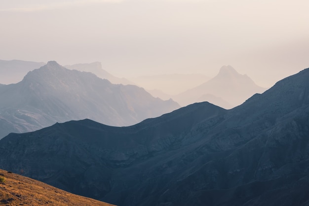 Weicher Fokus. Malerische Morgendämmerung Berglandschaft mit leichtem Nebel im Tal zwischen Bergsilhouetten unter bewölktem Himmel. Lebendige Sonnenuntergangs- oder Sonnenaufgangslandschaft mit niedrigen Wolken im Bergtal in sanften Farben.