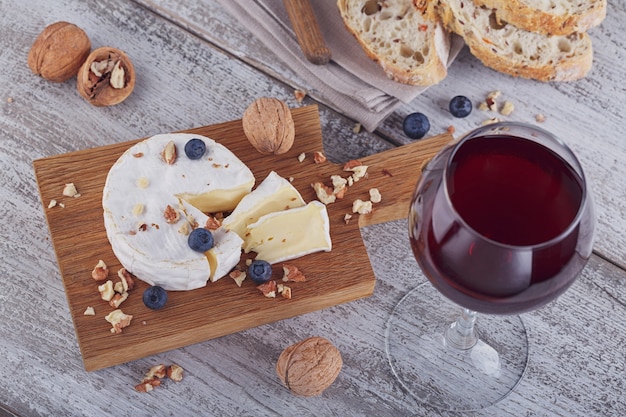 Weicher französischer Camembertkäse, serviert mit gehackten Walnüssen, Glas Rotwein und Blaubeeren auf Holzplatte.