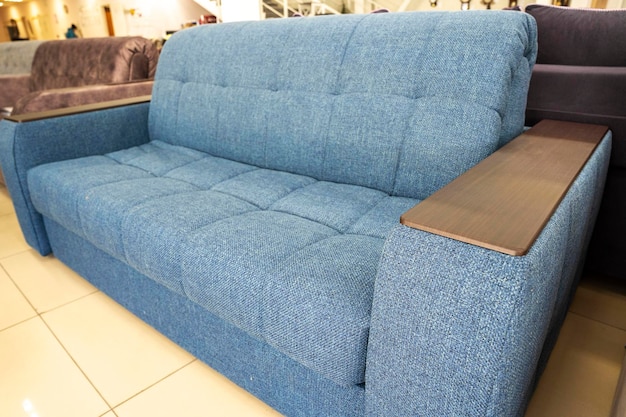 Weiches, neues, blaues, modernes, bequemes Sofa mit hölzerner Armlehne, Nahaufnahme und Design von Polstermöbeln