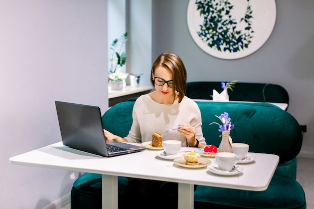 Weichzeichnung schoss von der Frau am coworking Raum oder am Café mit Internetanschluss, arbeitet an Laptop und genießt die Nachtische und wartet auf Kunden. Konzentriert bei der Arbeit.