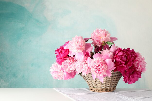 Weidenkorb mit Blumenstrauß der schönen Pfingstrosen auf weißem Tisch gegen blauen Hintergrund