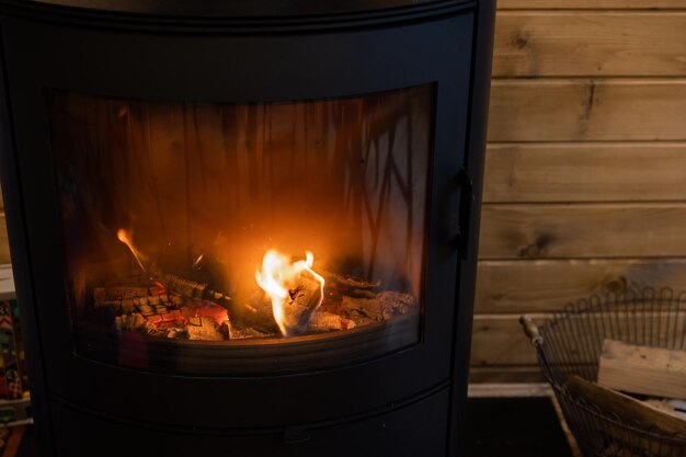 Weidenkorb mit Brennholz in der Nähe des Feuerkamins Holzofenkamin mit Metallkörper und Glastür im Komforthaus mit gemütlichem Interieur im Zimmer