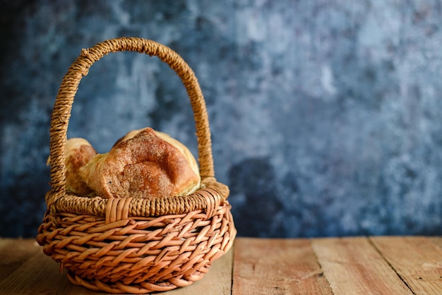 Weidenkorb mit süßem Brot auf Holztisch. Blauer Hintergrund.