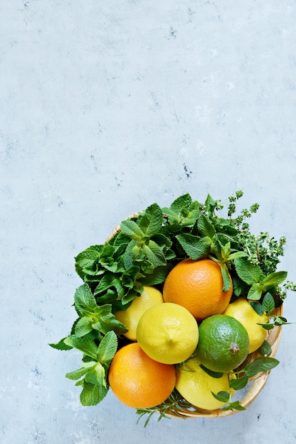 Weidenkorb mit Zitronen, Limetten, Orangen und frischer Minze auf blauem Hintergrund Obst-Zitrus-Set für die Herstellung frischer Sommerlimonade Platz für Textkopierraum