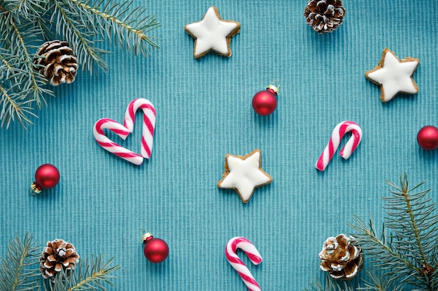 Weihnachten einfacher minimaler Hintergrund mit Tannenzweigen Zuckerstangen Tannenzapfen Sternkekse Frohe Weihnachten und frohe Feiertage Flach lag Draufsicht auf türkisfarbenem Holz