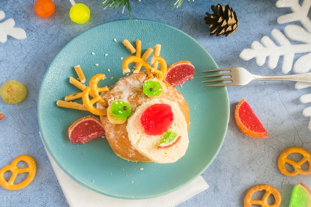 Weihnachten essbare Hirsche aus Brötchen und Marmelade auf einem blauen Teller auf dem Feiertagstisch neben Süßigkeiten